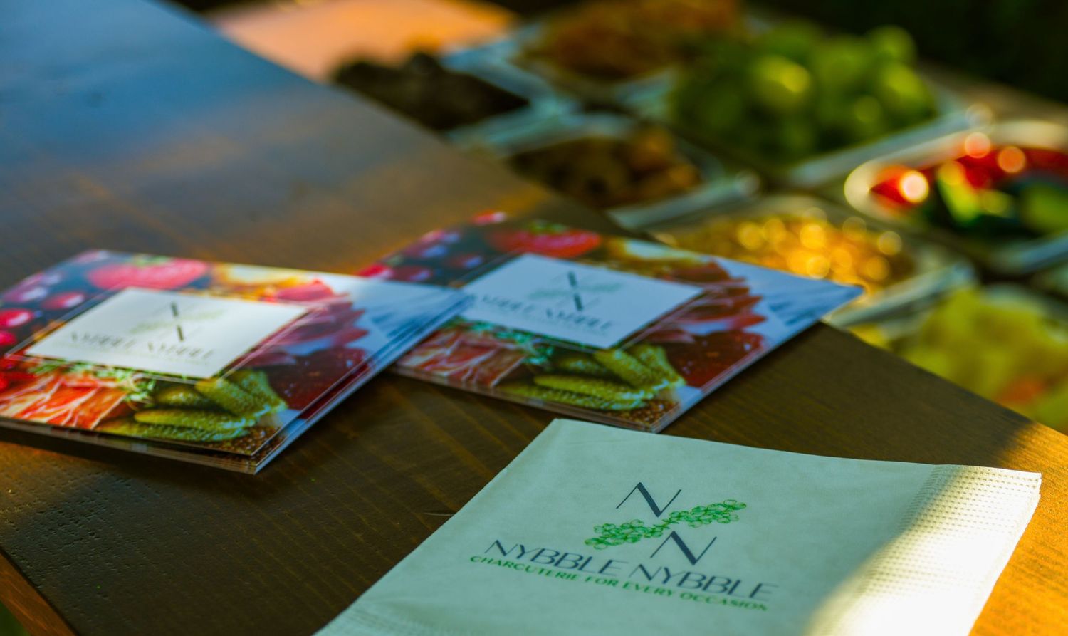Catered event table with Nybll branded napkins, menus and colorful food platters on display.