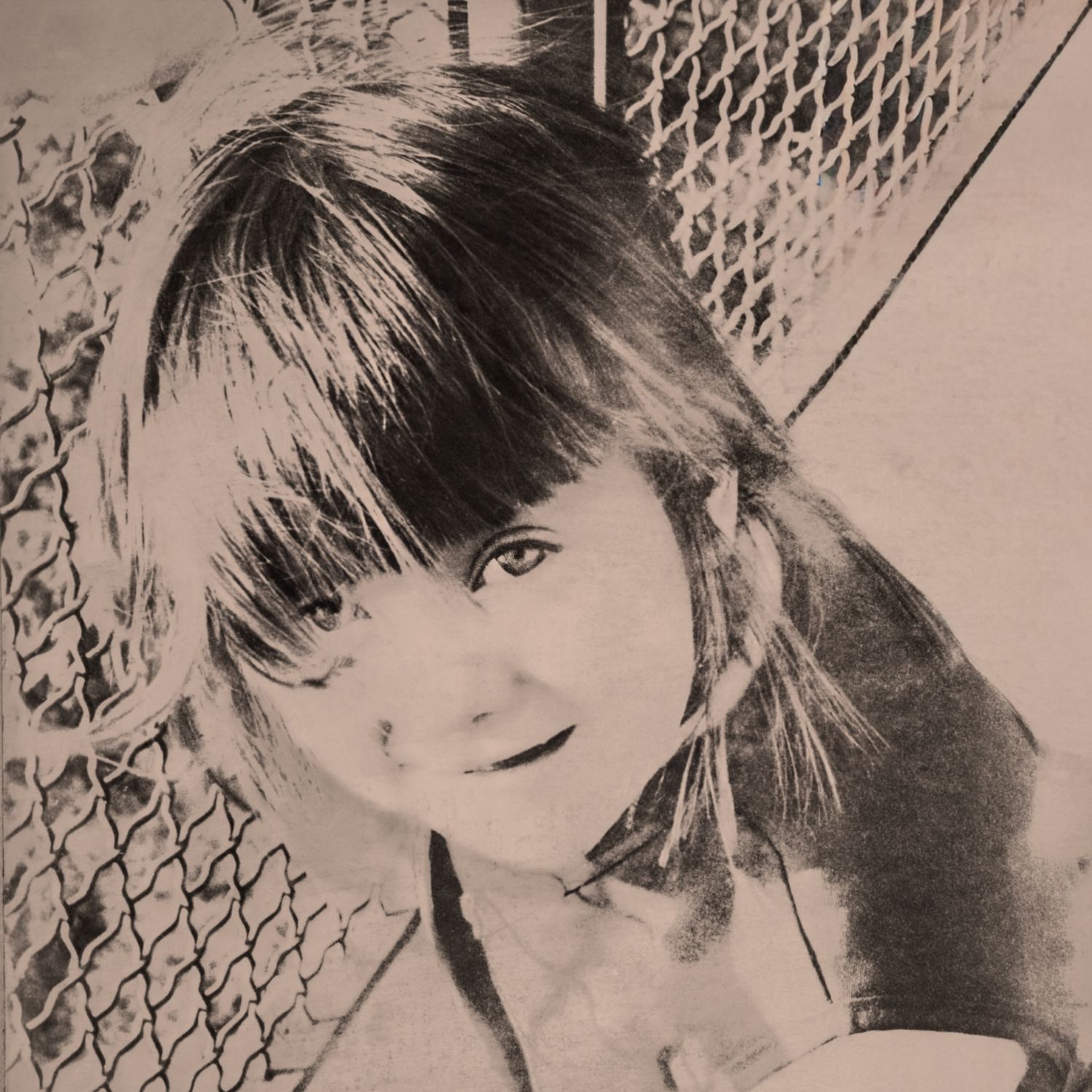 Vintage black and white portrait of a young girl with bangs smiling near a chain-link fence.