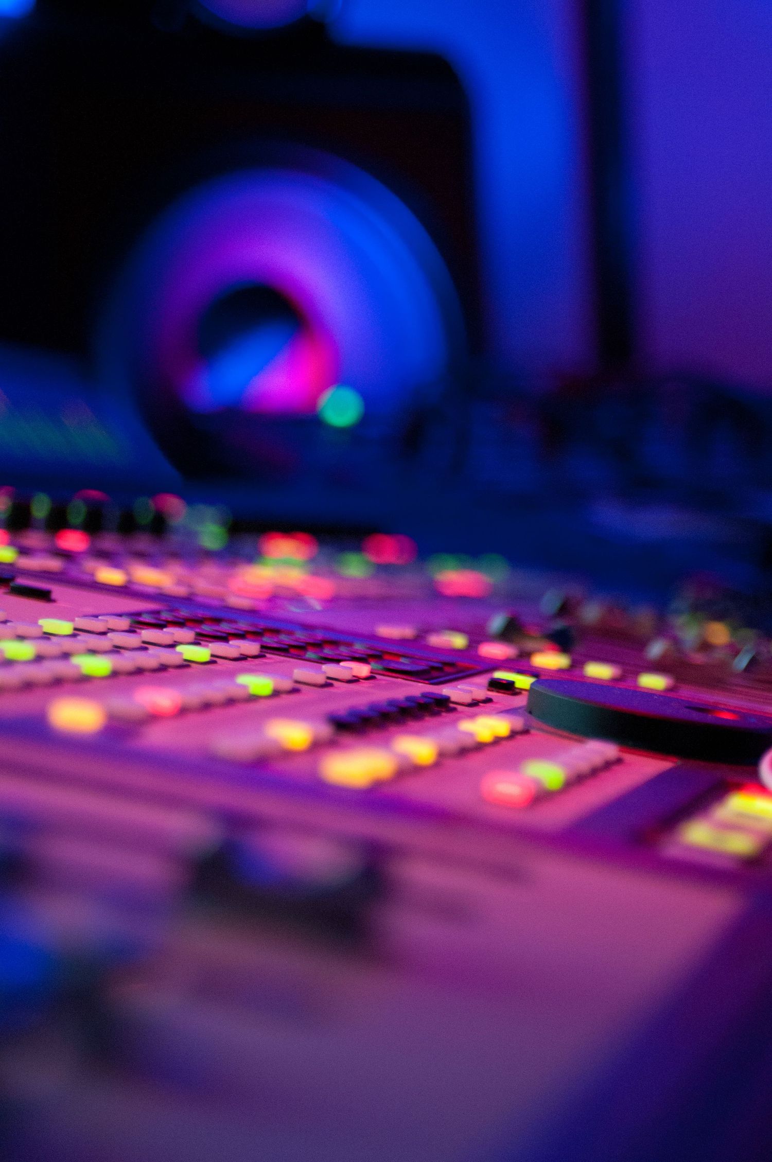Close-up of a professional audio mixing console with colorful glowing buttons in a dark studio.
