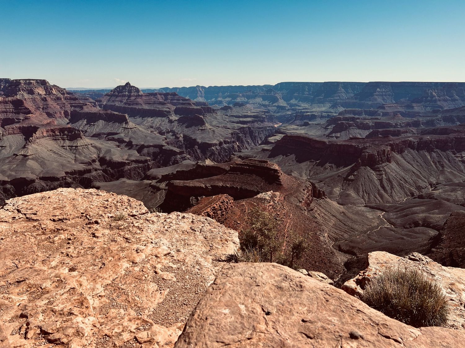 Panoramic view of the Grand Canyon's layered red rock formations under a clear blue sky from the South Rim.