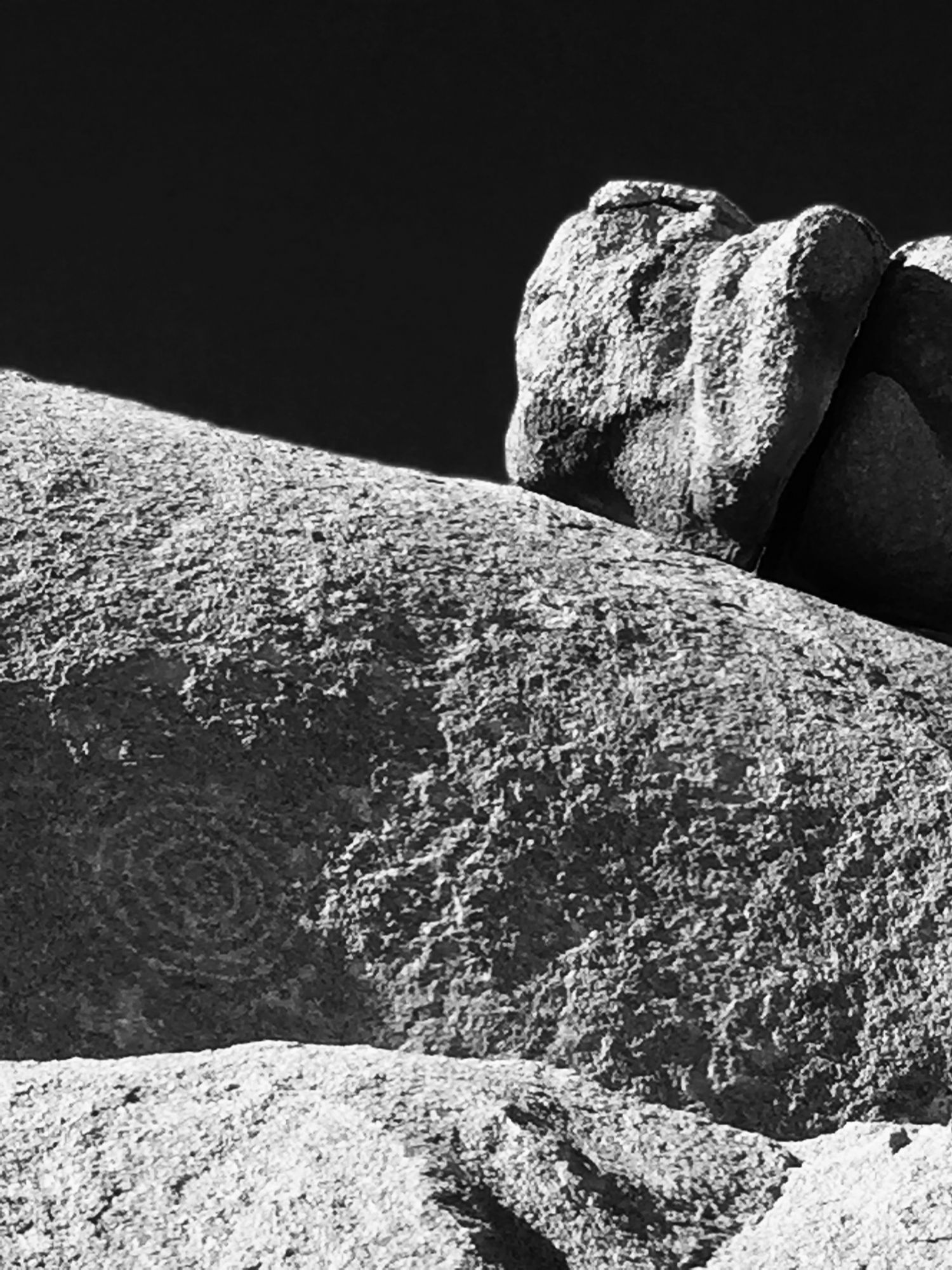 Black and white close-up of large granite boulders with a spiral petroglyph carved into the rock surface.