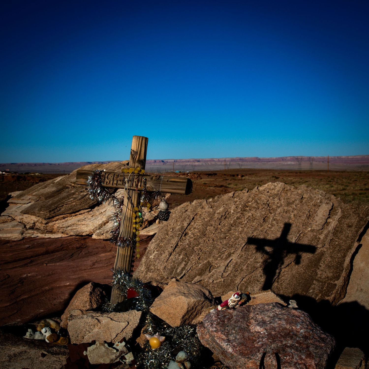 Decorated wooden memorial cross with flowers on rocky desert terrain under a clear blue sky.