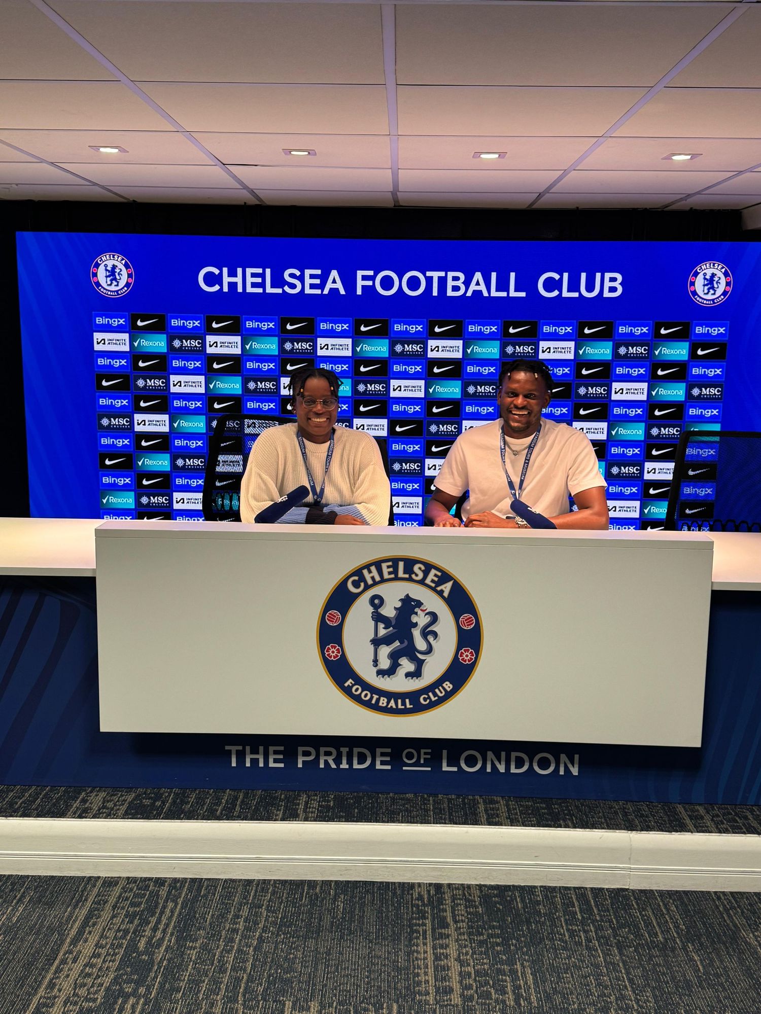 Two people sitting at Chelsea Football Club press conference table at Stamford Bridge stadium.