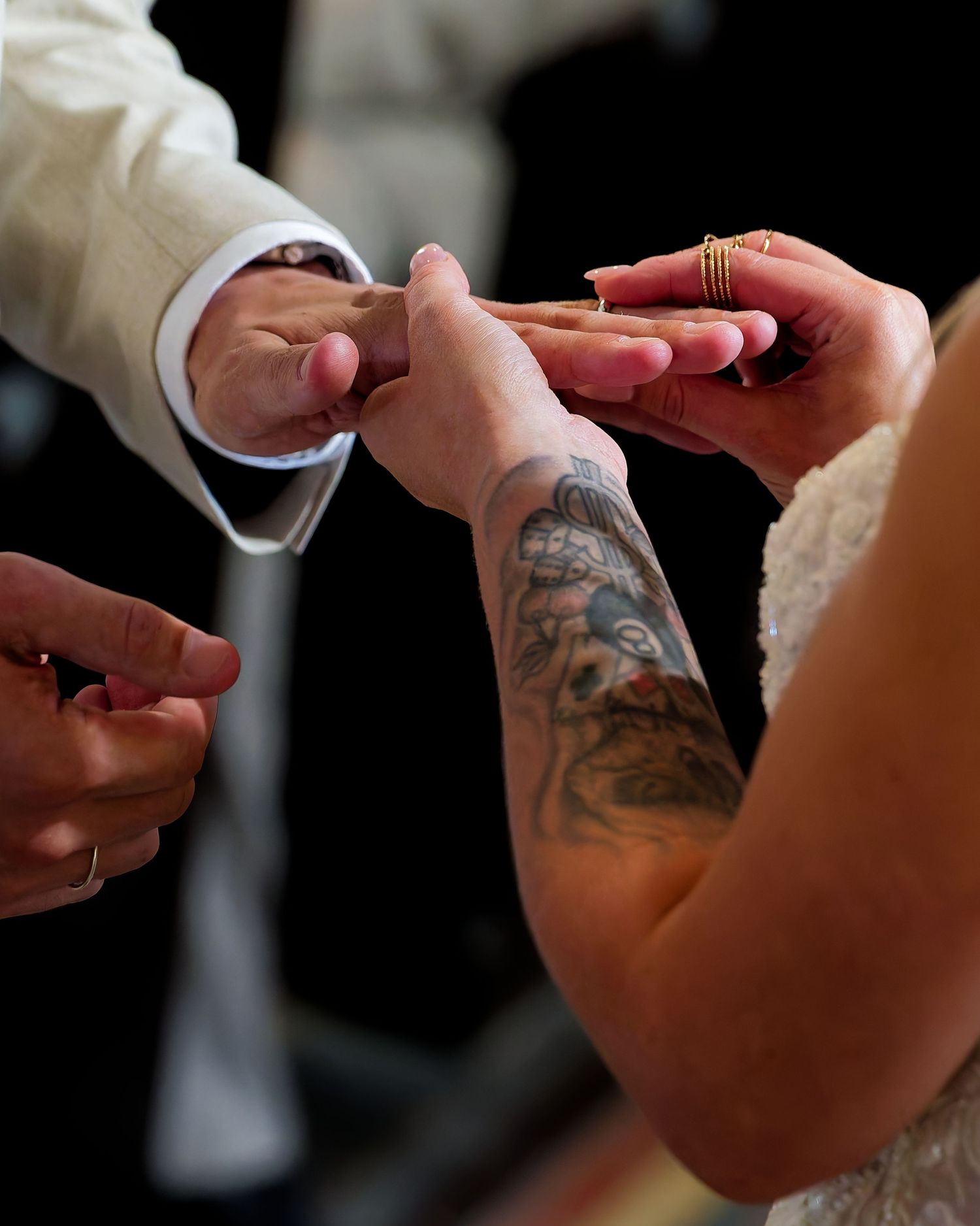 Bride with tattoo sleeve exchanging wedding rings with groom during ceremony.