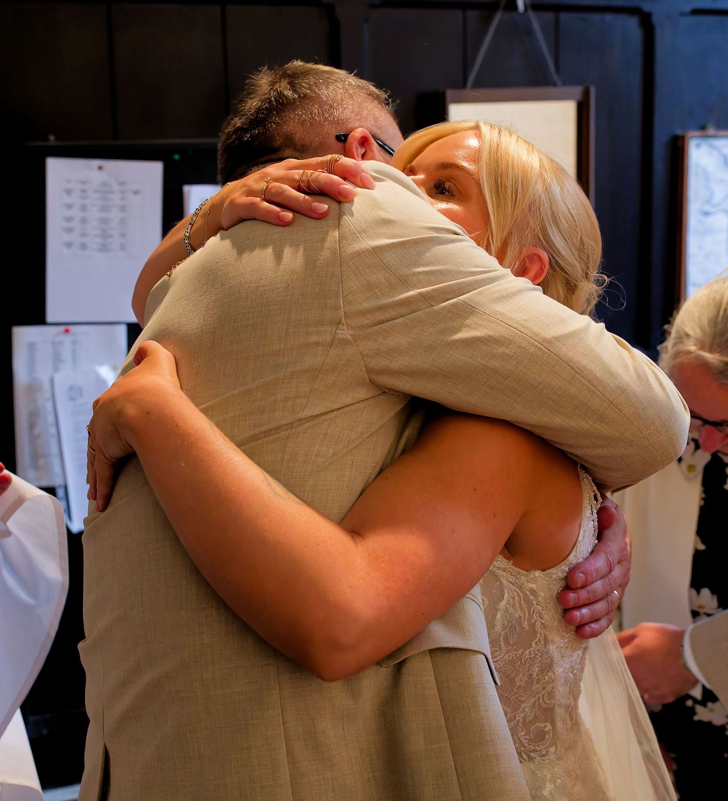 Two people sharing an emotional hug at a wedding ceremony, dressed in formal attire.