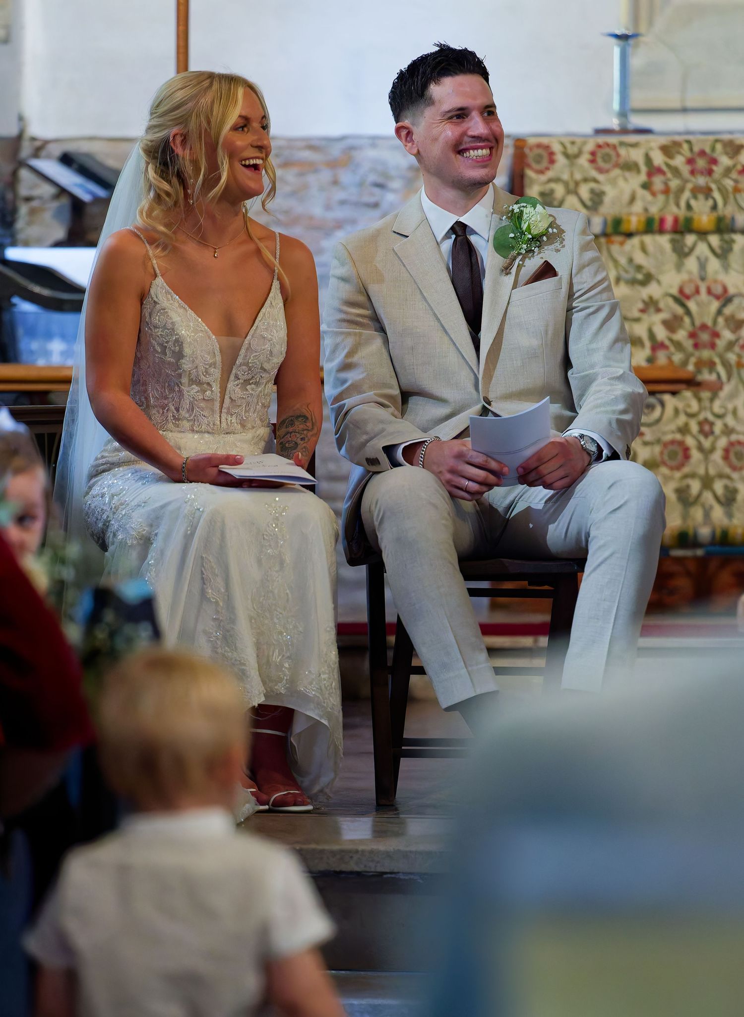 Bride and groom seated together laughing joyfully during their wedding ceremony in a church.