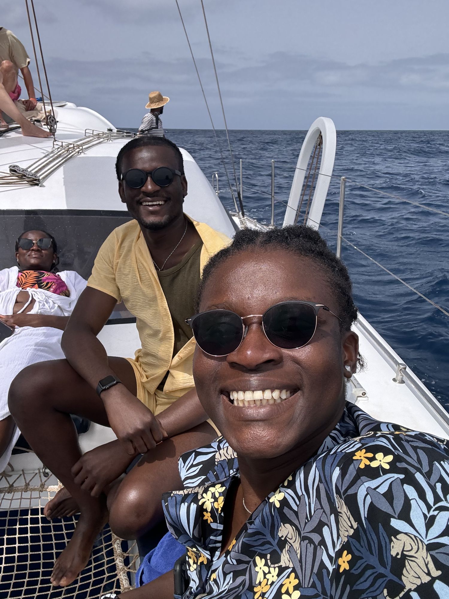 Group of friends smiling and relaxing on a sailing catamaran on the open ocean.