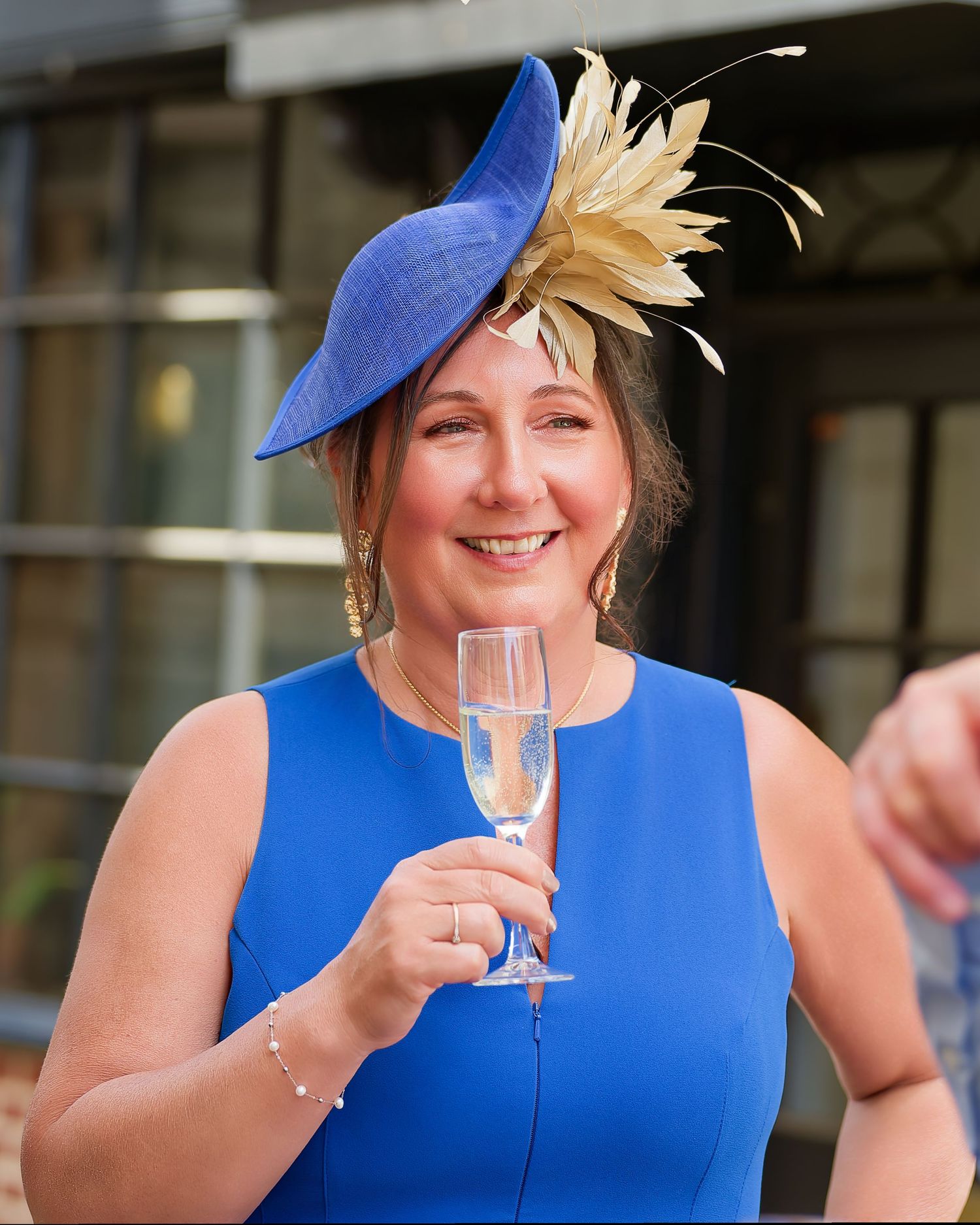 Elegant woman in blue dress and matching fascinator hat holding champagne glass at a formal event.
