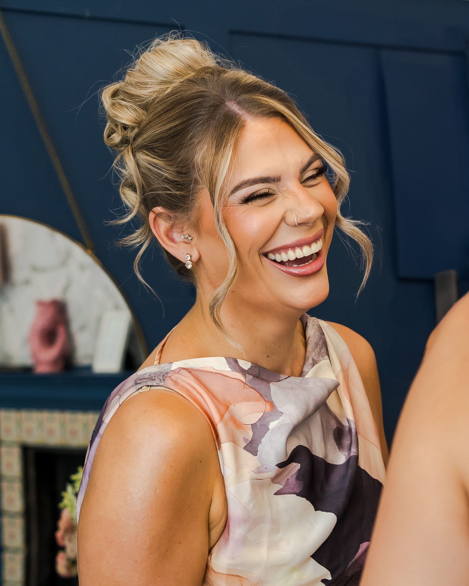 Beautiful smiling bridesmaid with an elegant updo hairstyle laughing joyfully at a wedding celebration indoors.