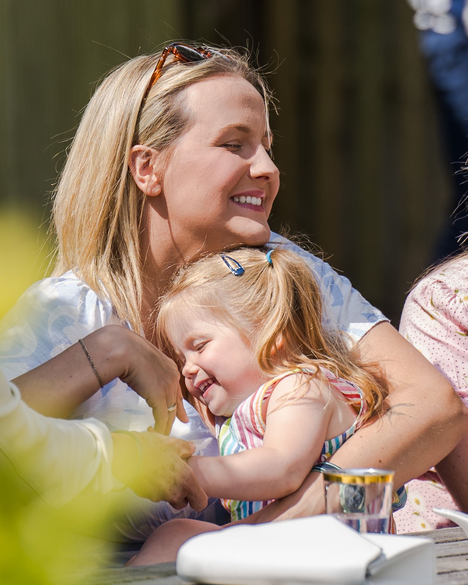 A tender moment is shared between parent and child as they embrace and laugh together outdoors on a sunny day.