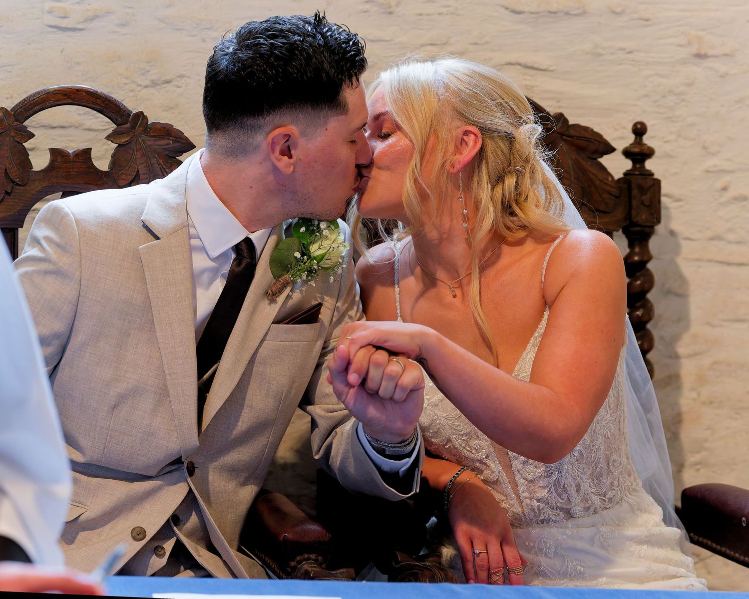 Newlywed couple sharing a romantic kiss at their wedding reception, bride in white lace gown, groom in light suit.