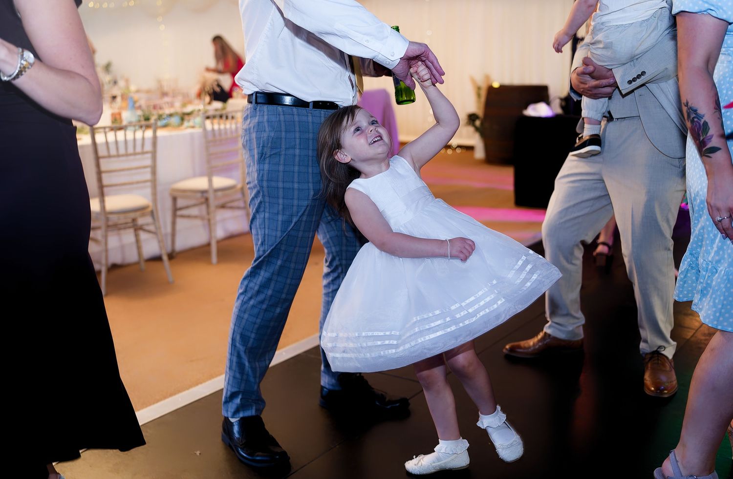 Young flower girl in white dress twirls on wedding reception dance floor with adult partner.