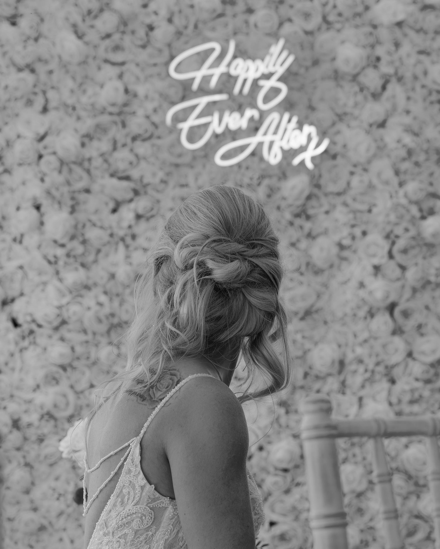 Black and white photo of bride with elegant updo hairstyle in front of Happily Ever After neon sign.