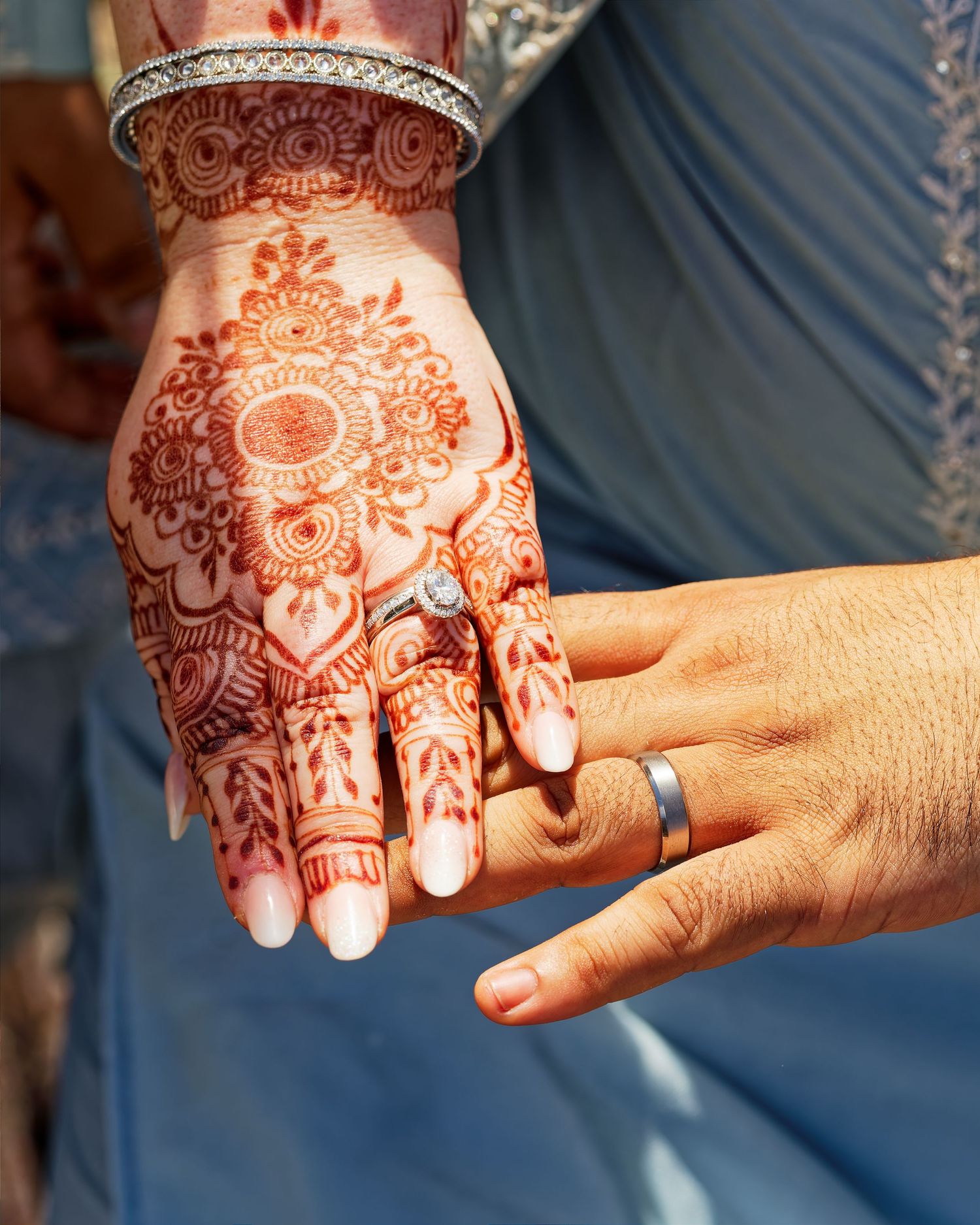 Close-up of bride's hand with intricate henna design and diamond ring held by groom at wedding.