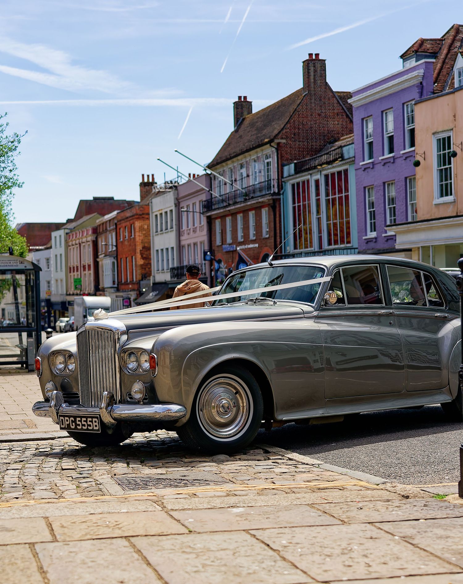 Vintage silver Bentley wedding car parked on cobblestone street with colorful Georgian buildings in background.