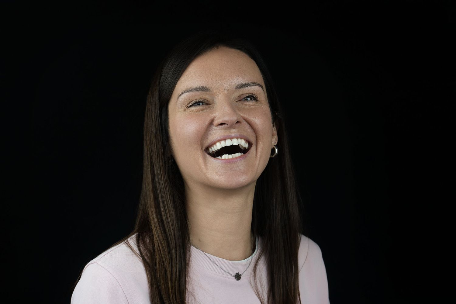 Joyful portrait of person with straight dark hair laughing against black backdrop.