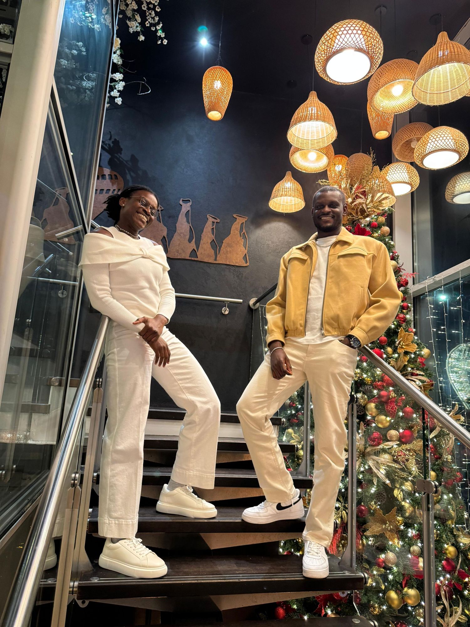 Stylish couple posing on stairs decorated with Christmas tree and pendant lights in a restaurant.