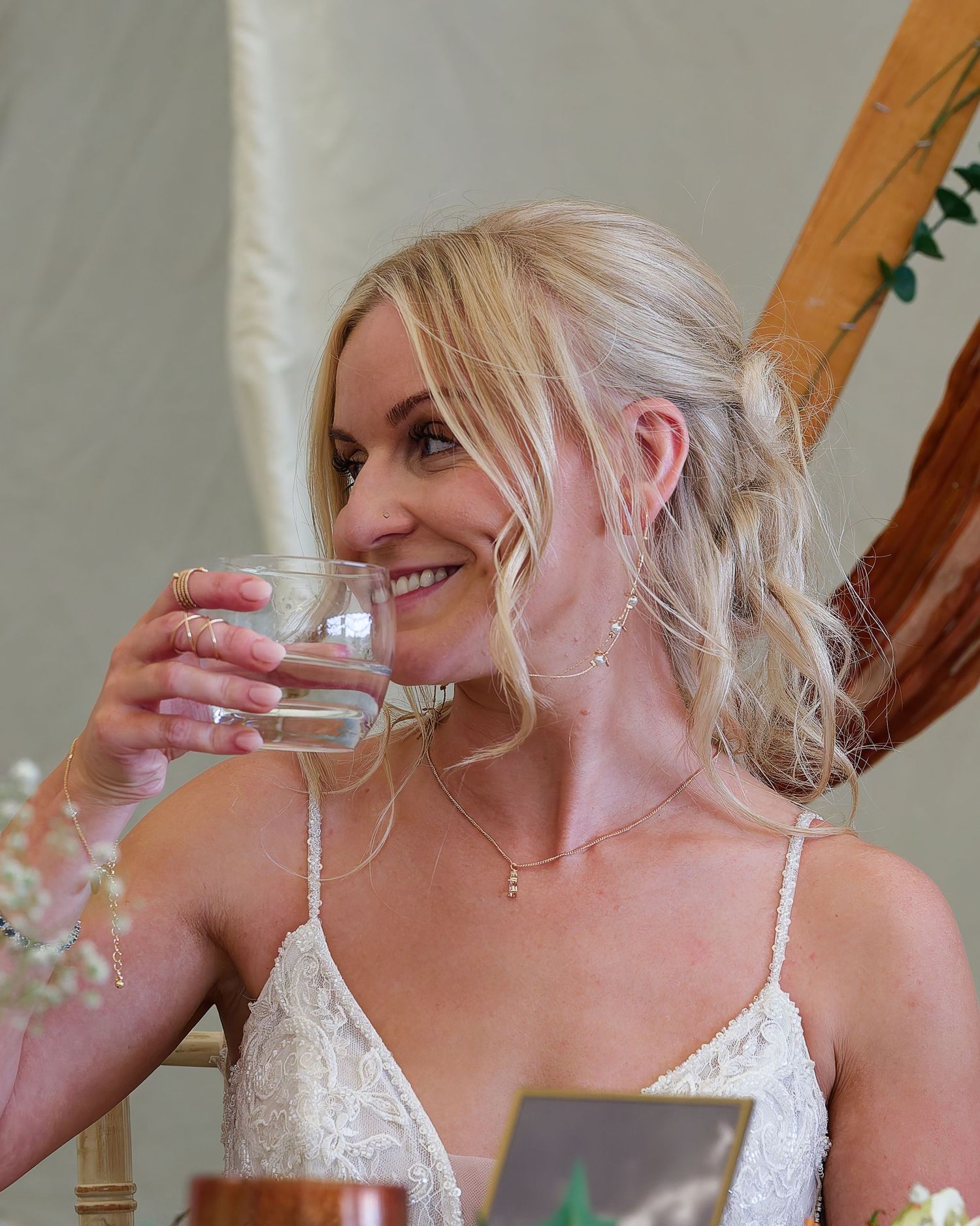 Beautiful blonde bride in lace wedding dress smiling while holding a glass at her wedding reception.