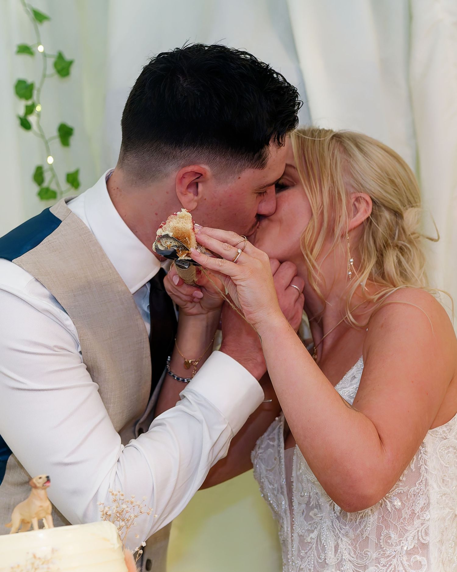 Bride and groom sharing a romantic kiss while cutting their wedding cake, dressed in elegant wedding attire.