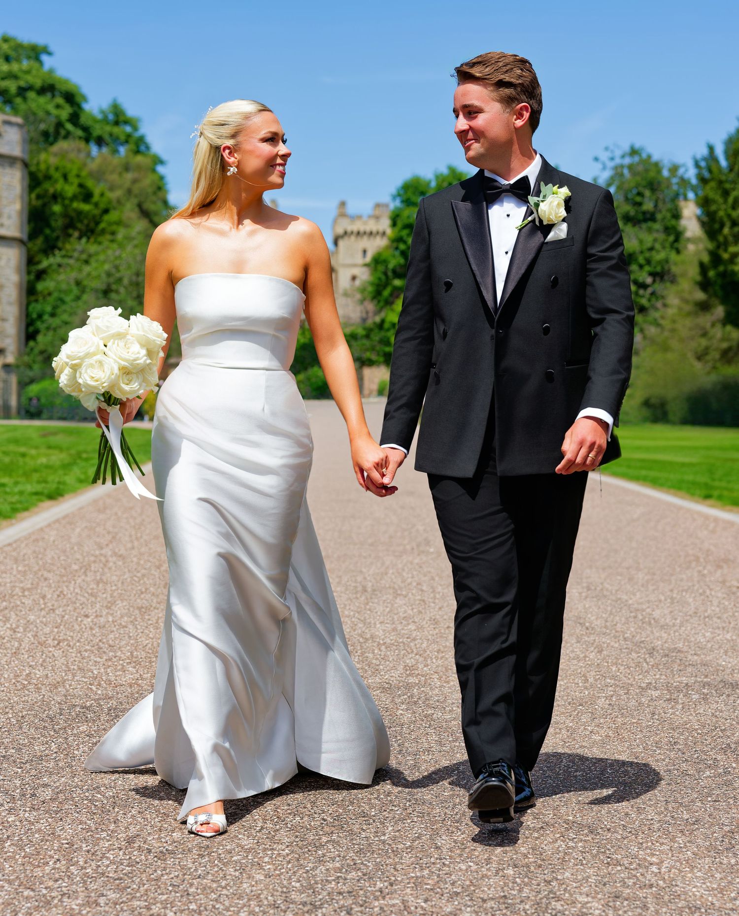 Bride and groom walking hand in hand on a sunny path at Windsor Castle on their wedding day.