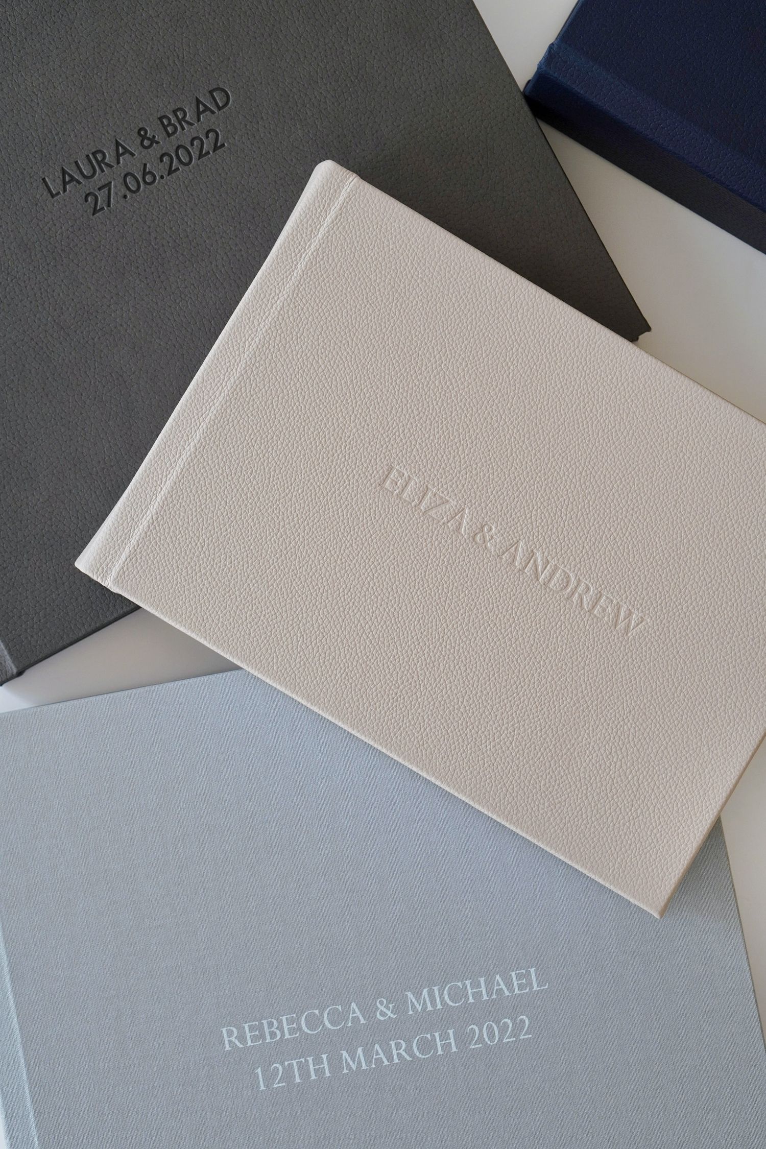 Three elegant embossed wedding guest books in cream, grey and blue with couples names and dates.