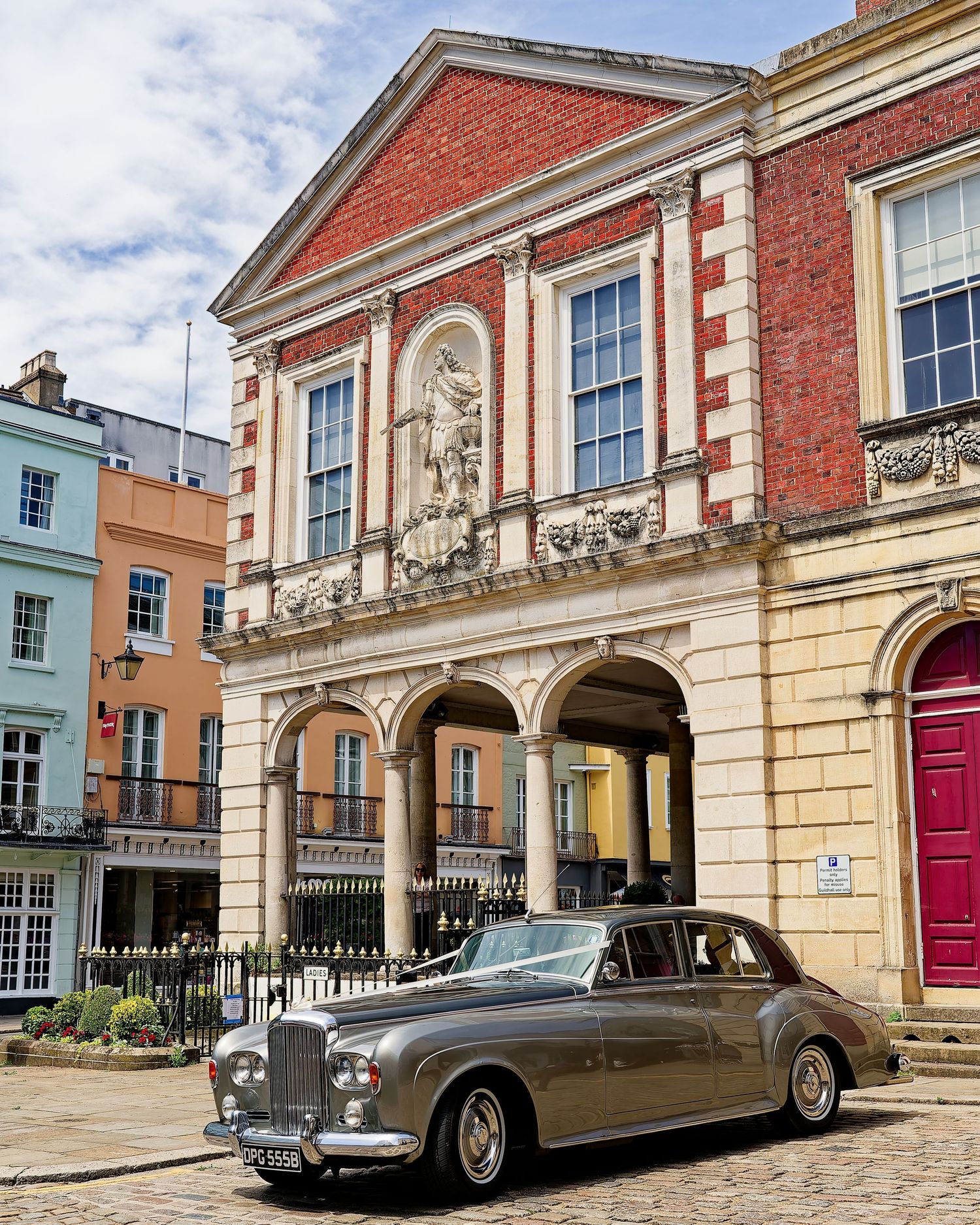 Vintage Rolls-Royce parked outside a Georgian red brick building with arched colonnade in a historic UK town square.