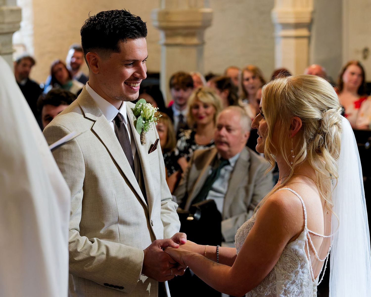 Bride and groom exchanging vows at elegant wedding ceremony with guests seated in ornate venue.