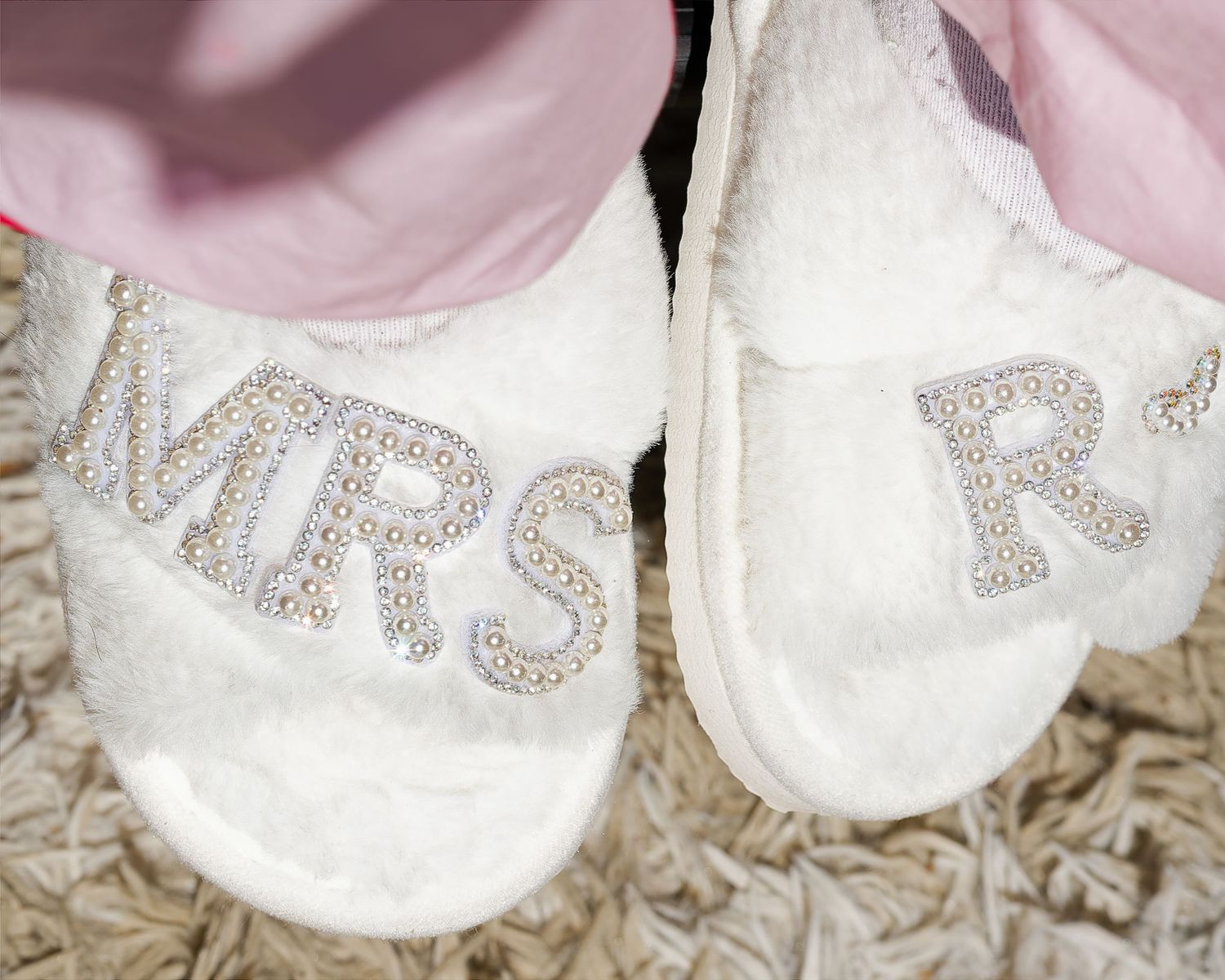 White fluffy bridal slippers decorated with pearl and crystal MRS rhinestone letters on a carpet.