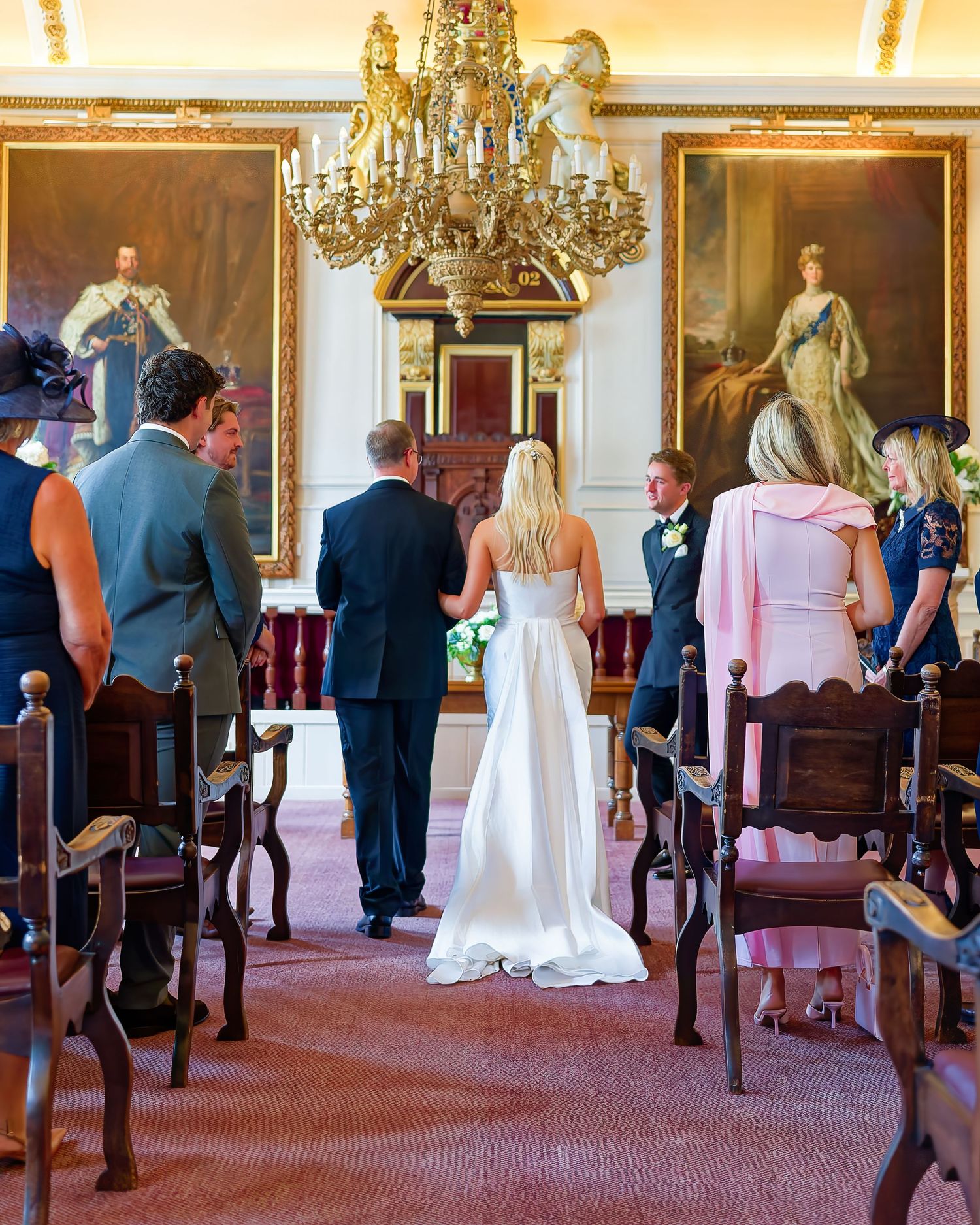 Elegant wedding ceremony in a grand hall with chandelier, oil paintings, and small intimate gathering.
