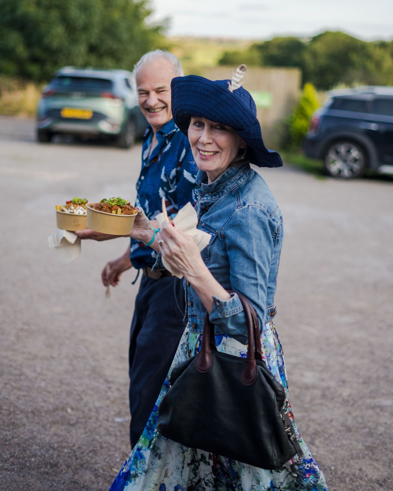 A couple in blue attire shares a joyful moment in a parking lot while holding food containers.