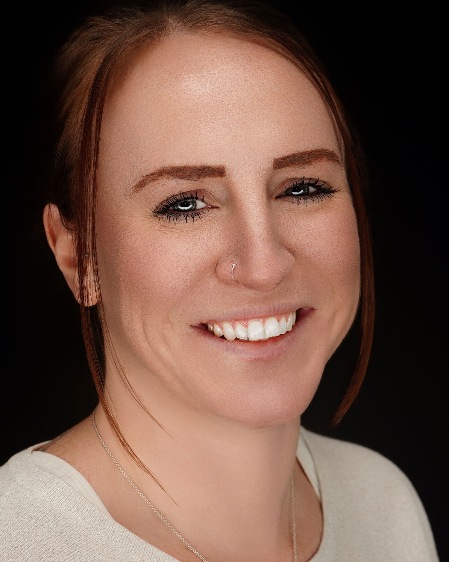 Professional studio portrait against black background showing bright smile and warm expression in a cream colored top.