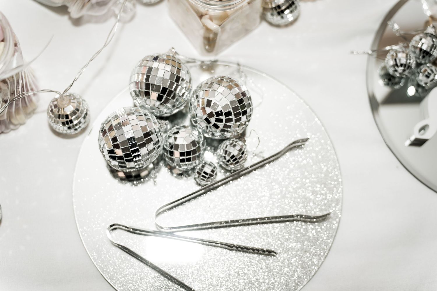 Silver mirror disco balls and cocktail stirrers arranged on a glittery plate for a glamorous wedding reception.