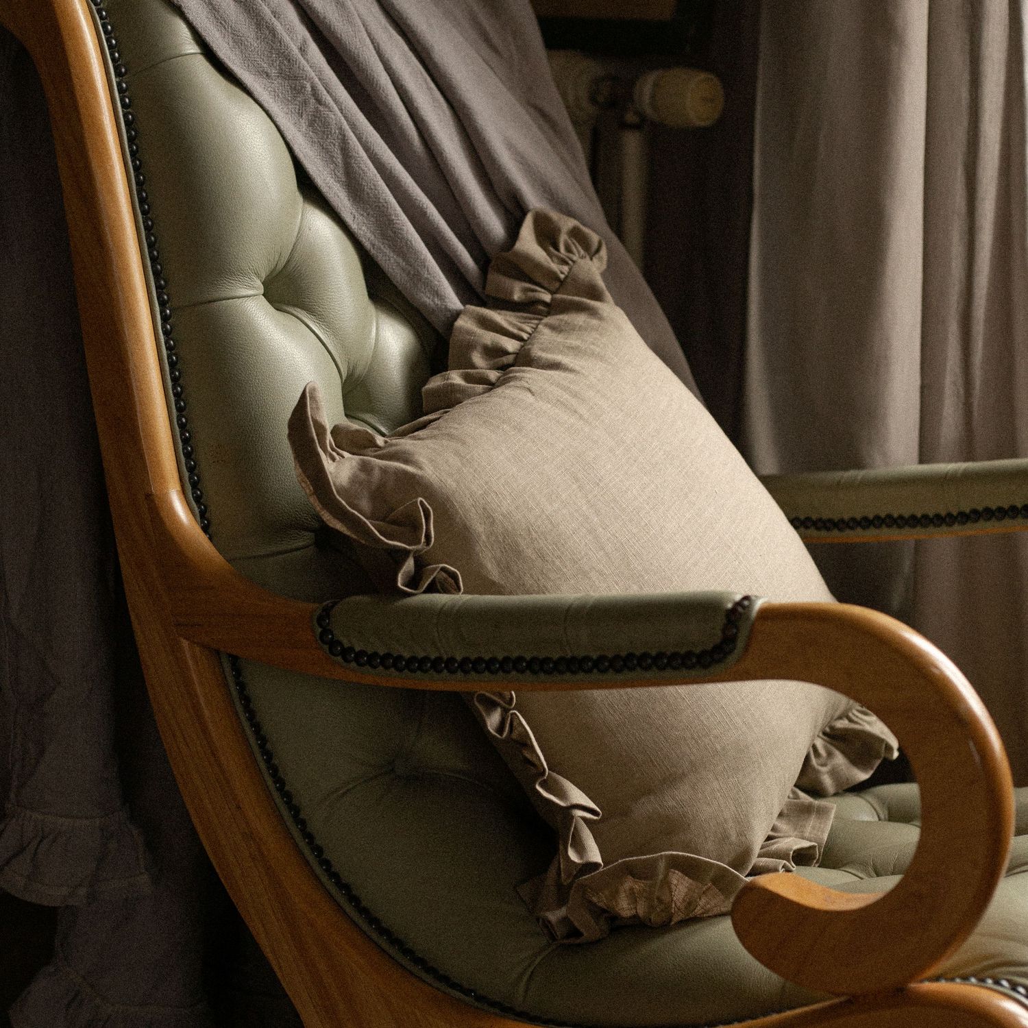green leather seat with grey linen throw and beige ruffled cushion
