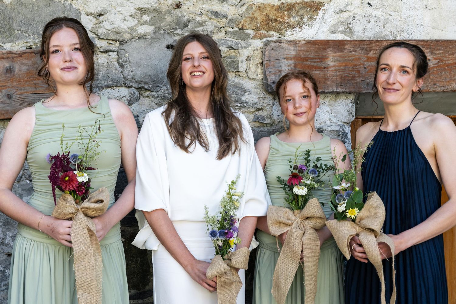 bride stands with bridesmaids and maid of honour holding wild flower bouquets