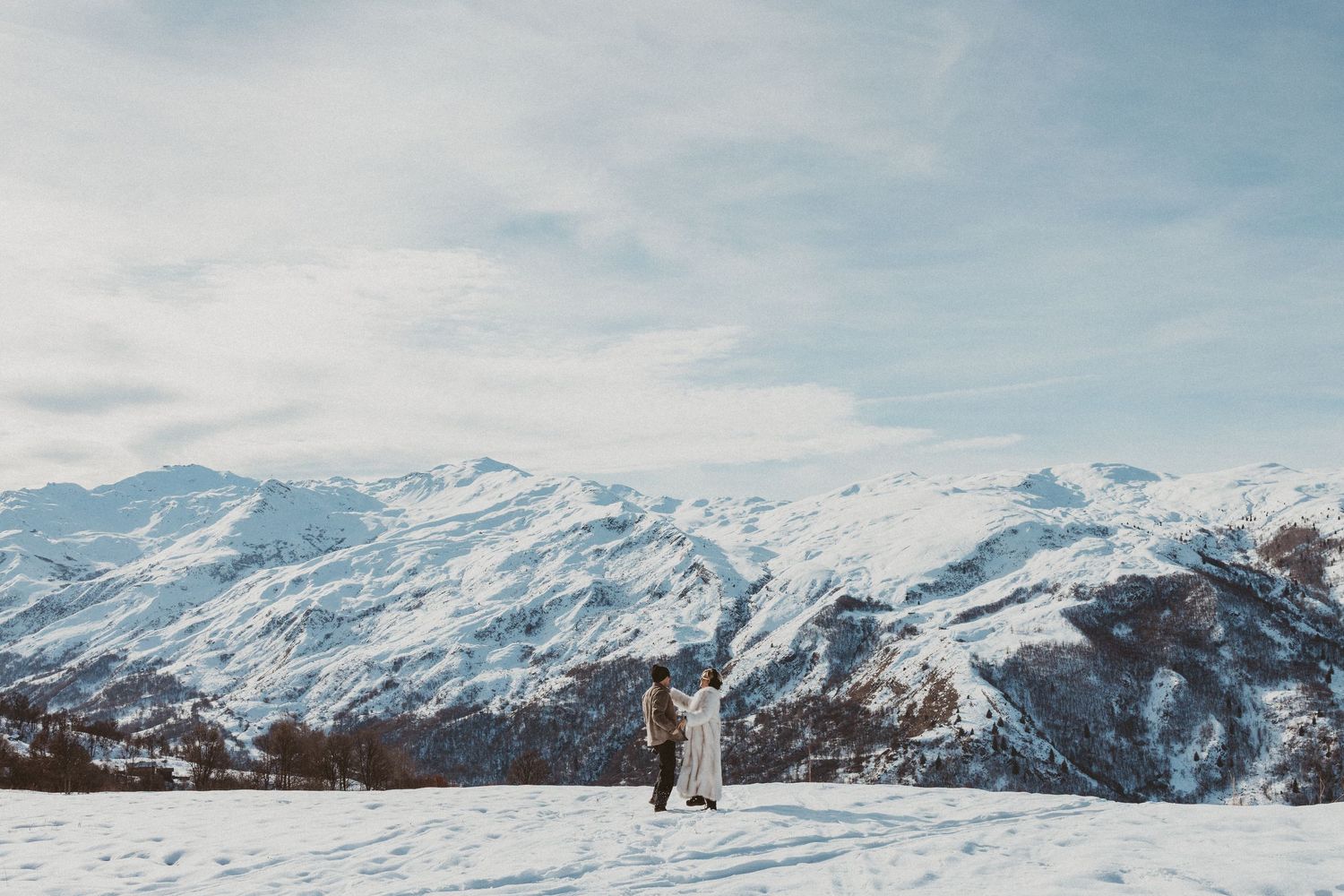 couple dances in front of snowy mountains during engagement