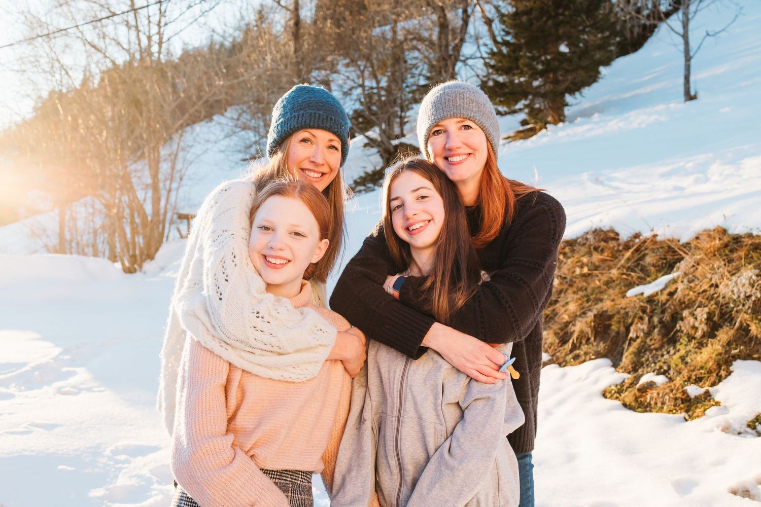 sisters embrace teenage daughters in snow during golden hour