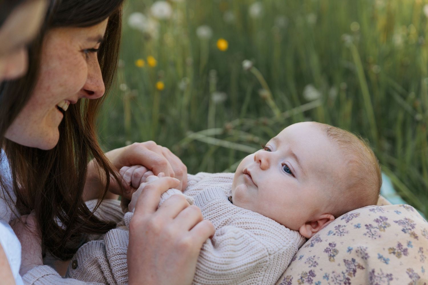 baby lies in parents lap in long grass