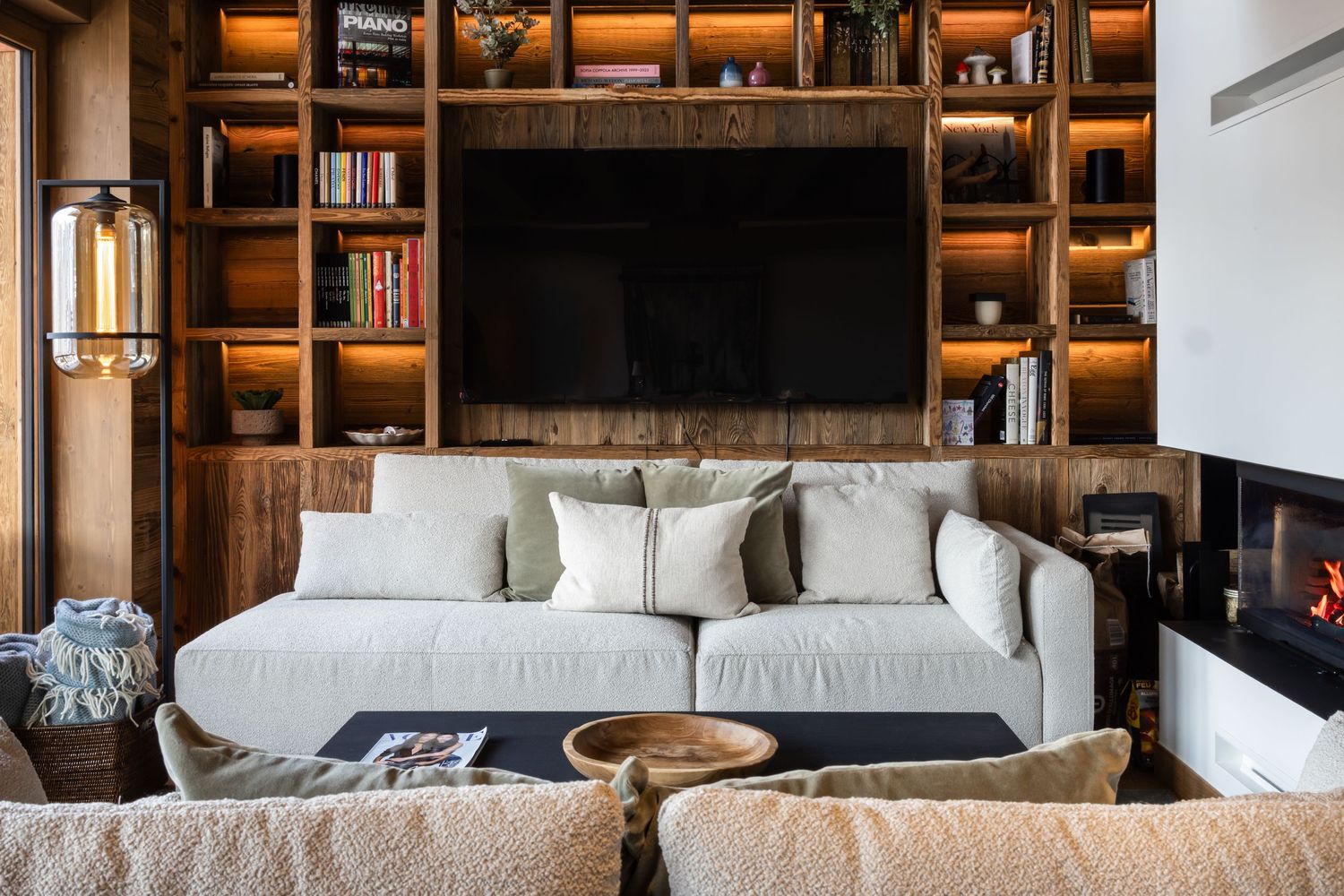 contemporary white sofa beside lit fireplace in front of media wall