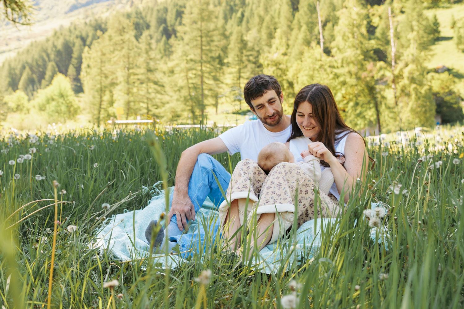 man and woman look lovingly at baby while sitting in long grass in the French alps