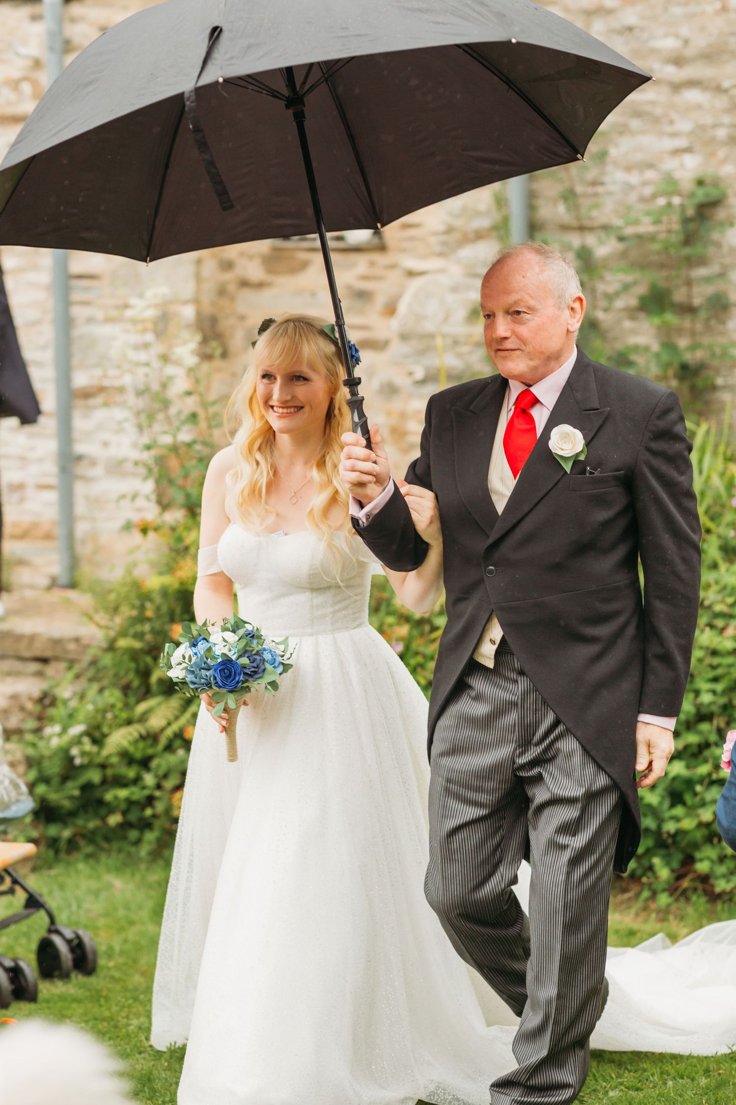 father of bride walks bride down aisle in garden weddings holding black umbrella
