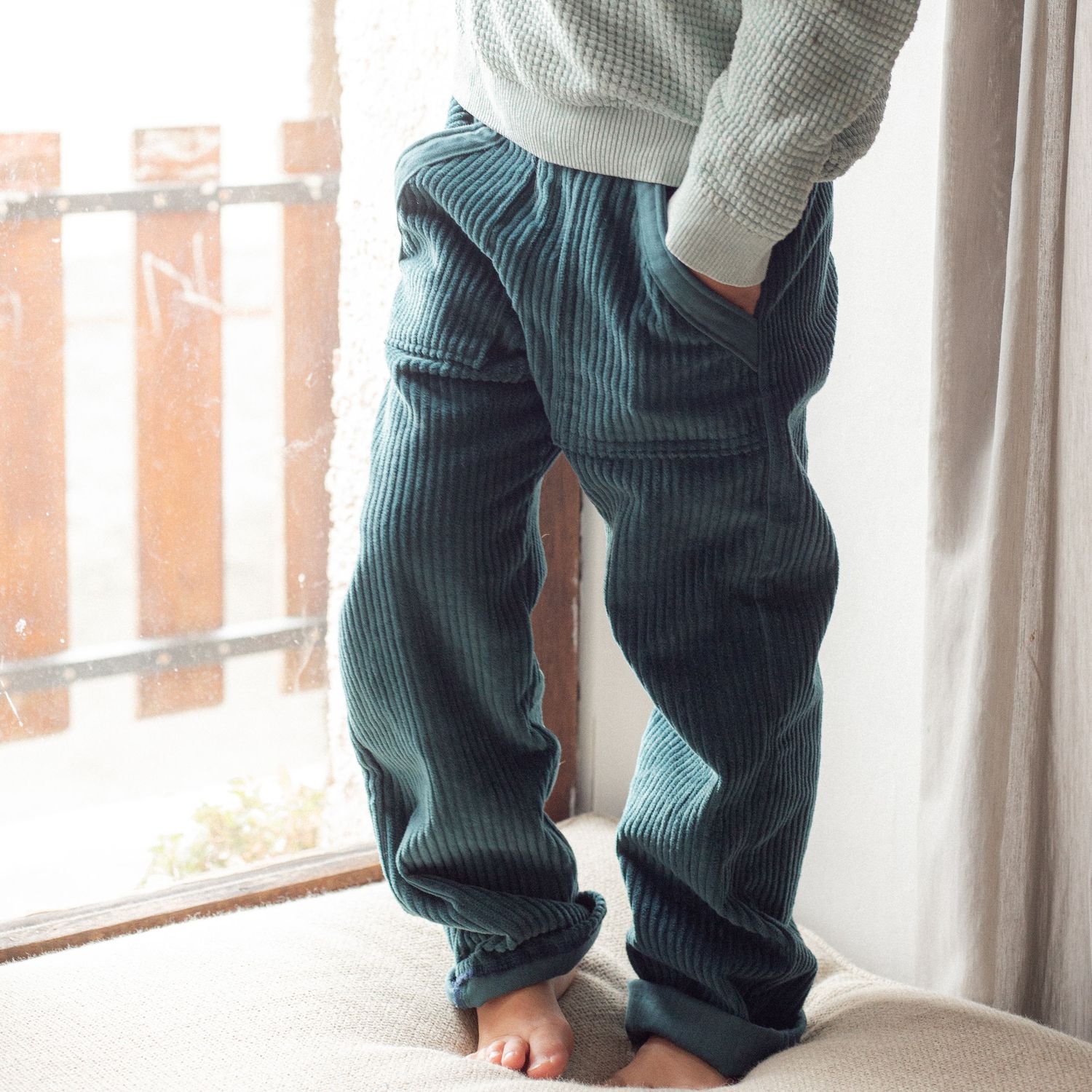 young child wearing navy blue corduroys in window
