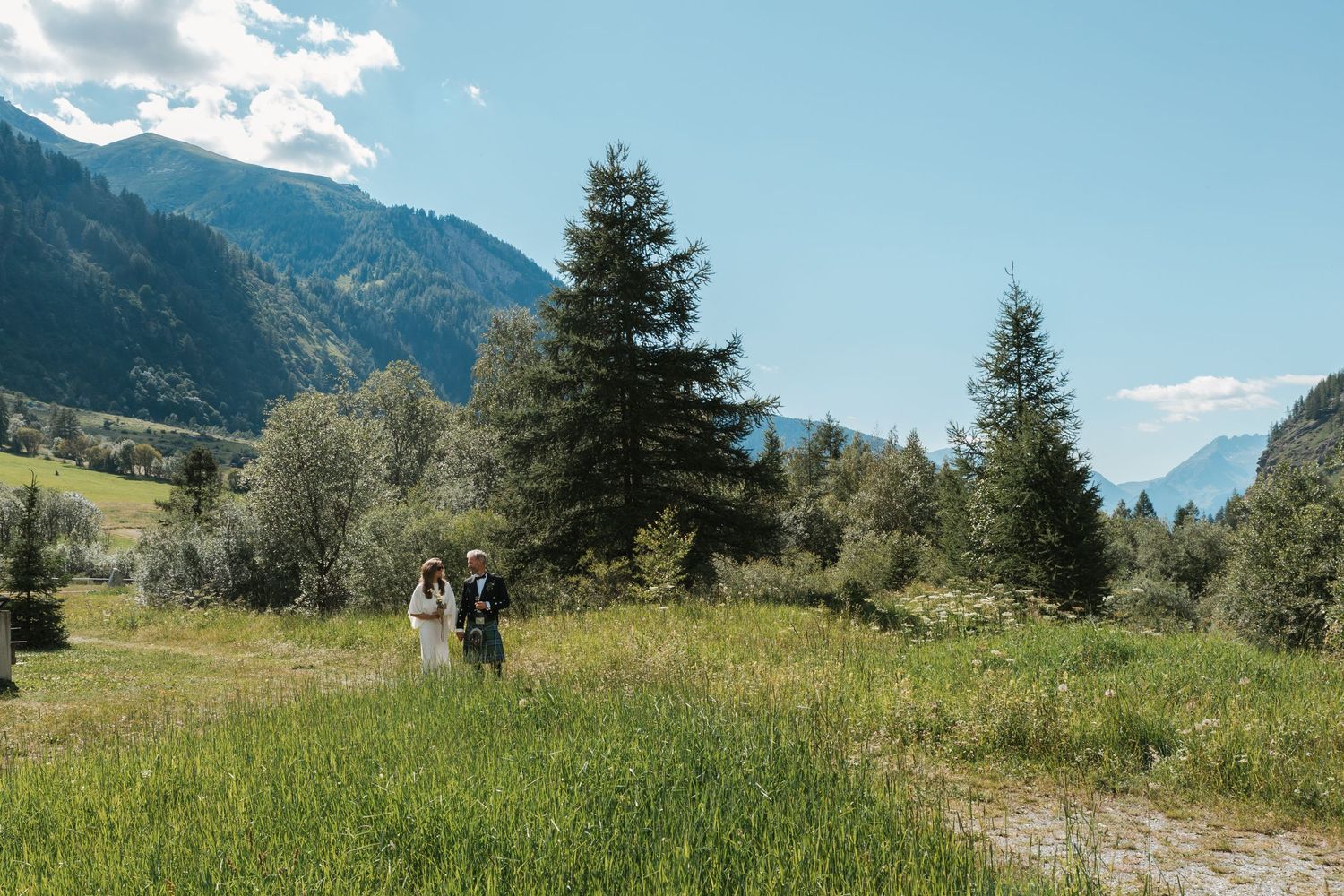 bride and groom walk through mountain meadow on sunny day
