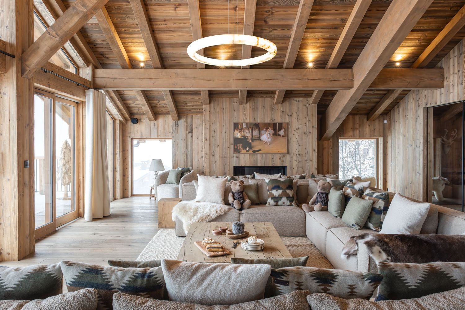 luxurious living space in ski chalet with bespoke ring light lit above as centerpiece. Large beige and green sofa with vintage teddies sitti