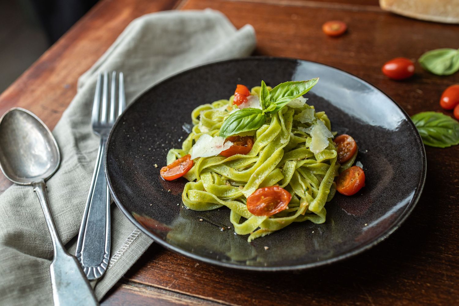black plate with green pasta served with basil and tomatoes