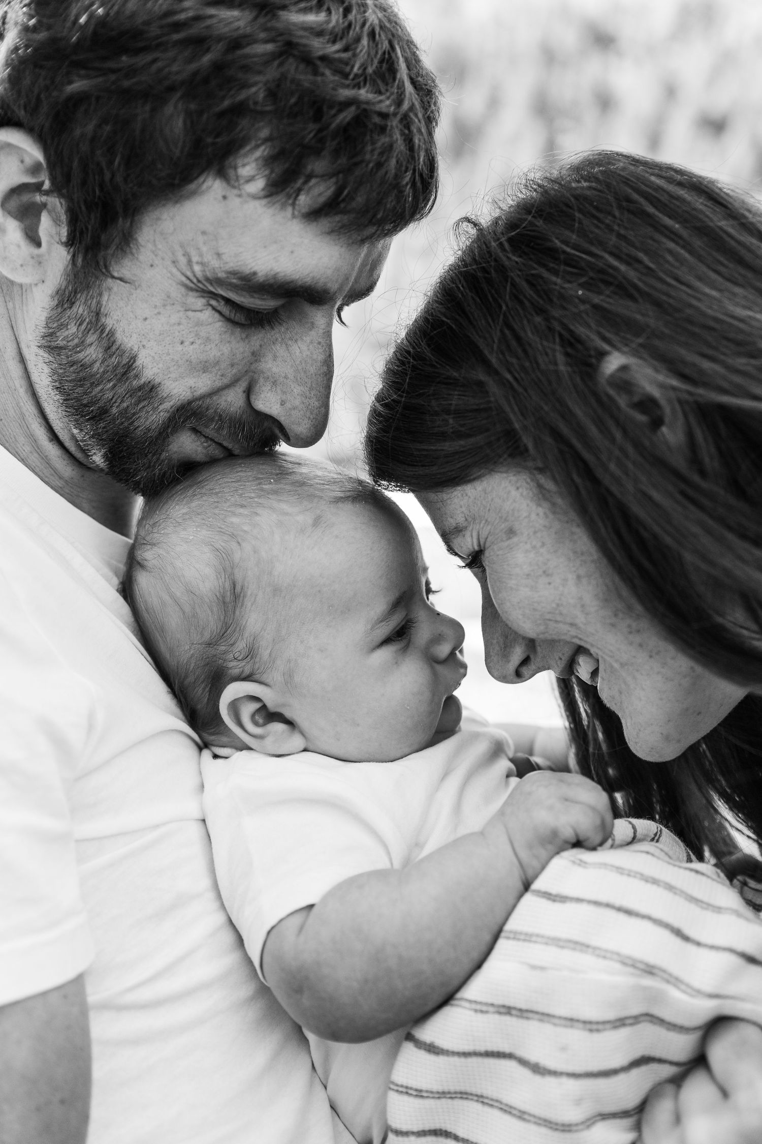 father holds infant son while mother moves closely to baby face