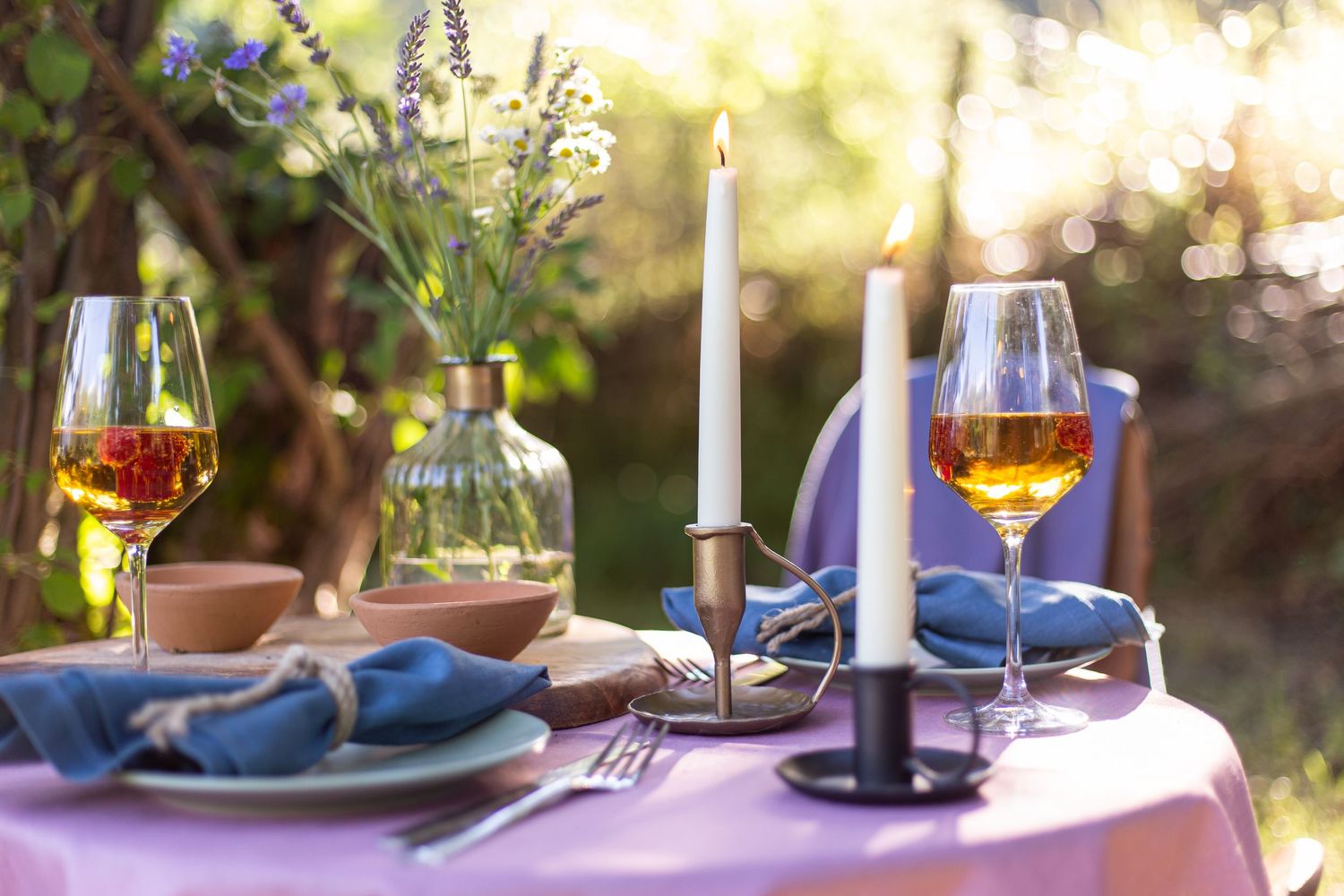 set table with candles, wine, plates and napkins on outside bistro table during golden hour