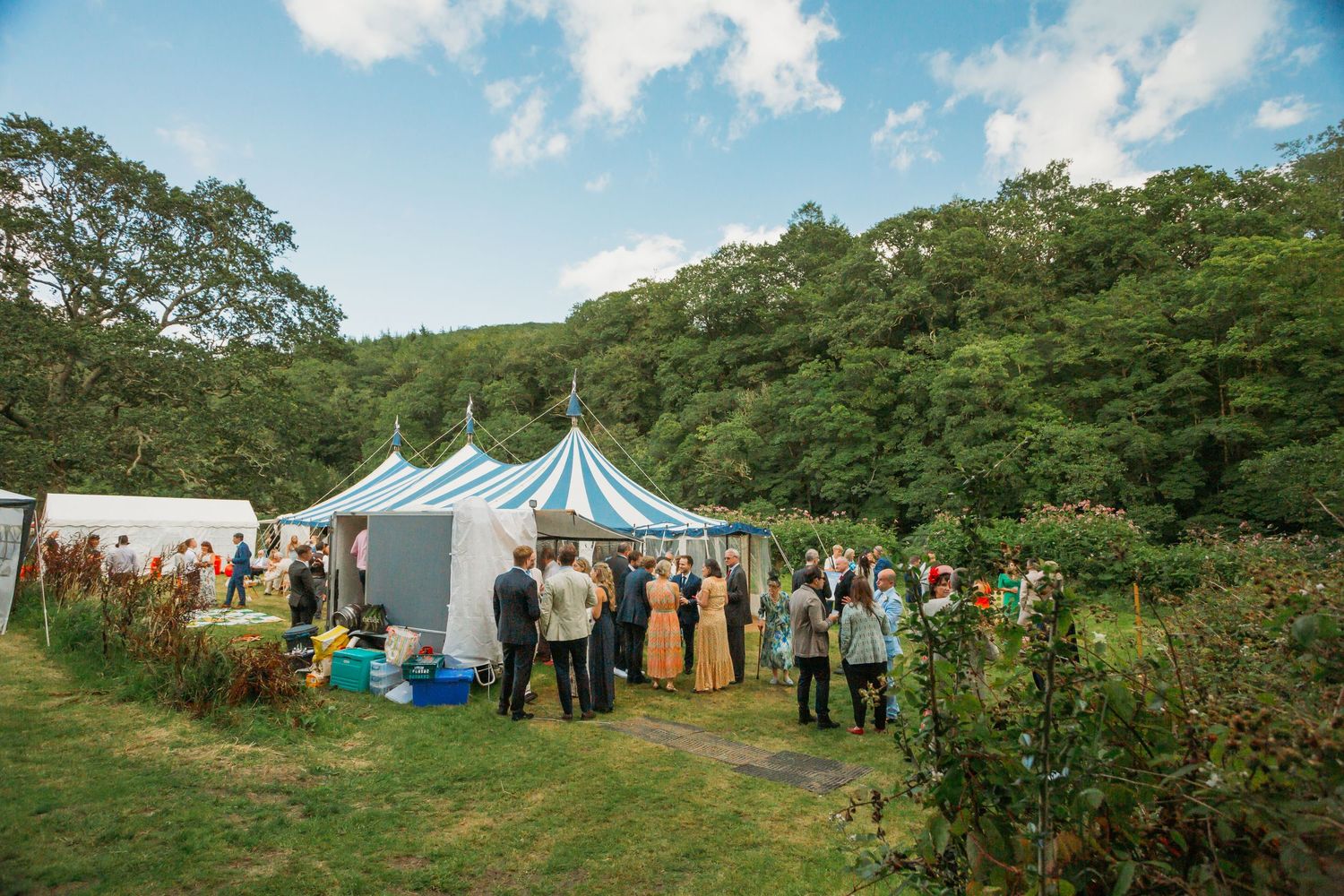 blue and white striped wedding marquee in field with wedding guests
