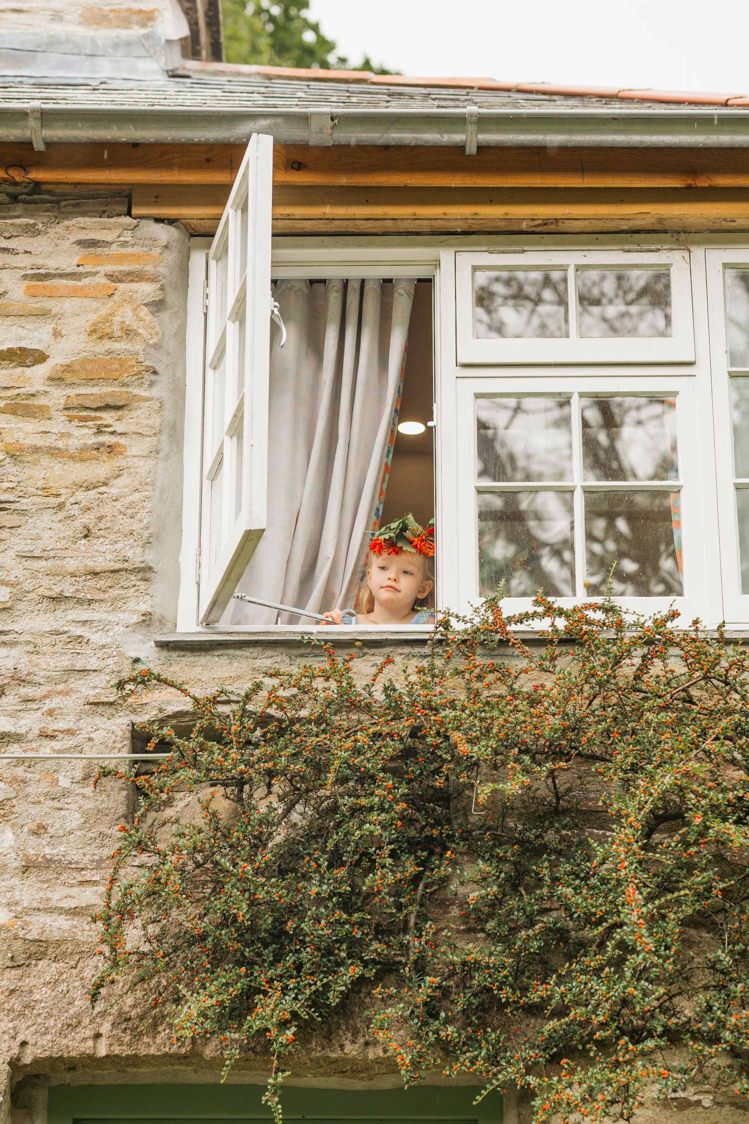 brides daughter peers out of upstairs window before wedding ceremony