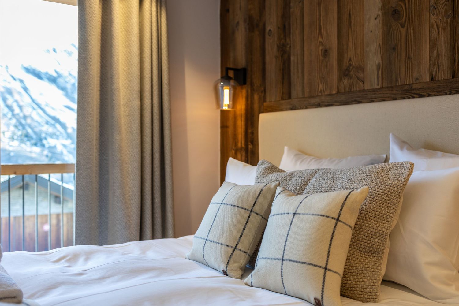 soft bed with pillows and throw cushions beside bedside wall lamp