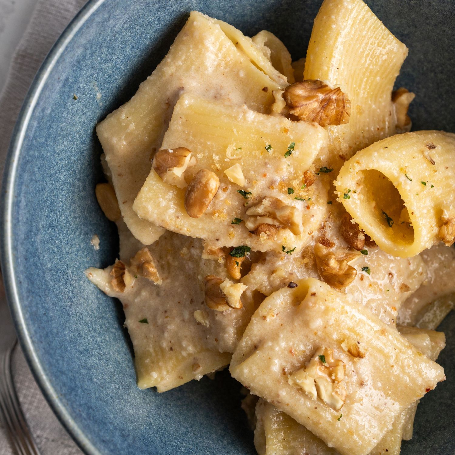 bowl of creamy cheese pasta decorated with walnuts in a blue bowl